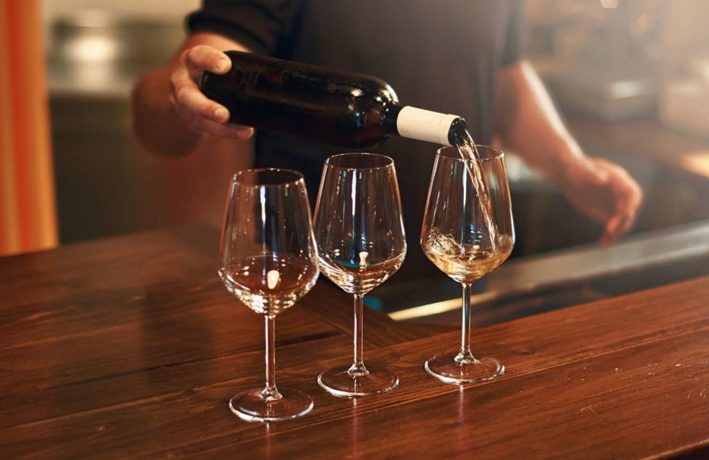 A waiter serving wine in three glases 