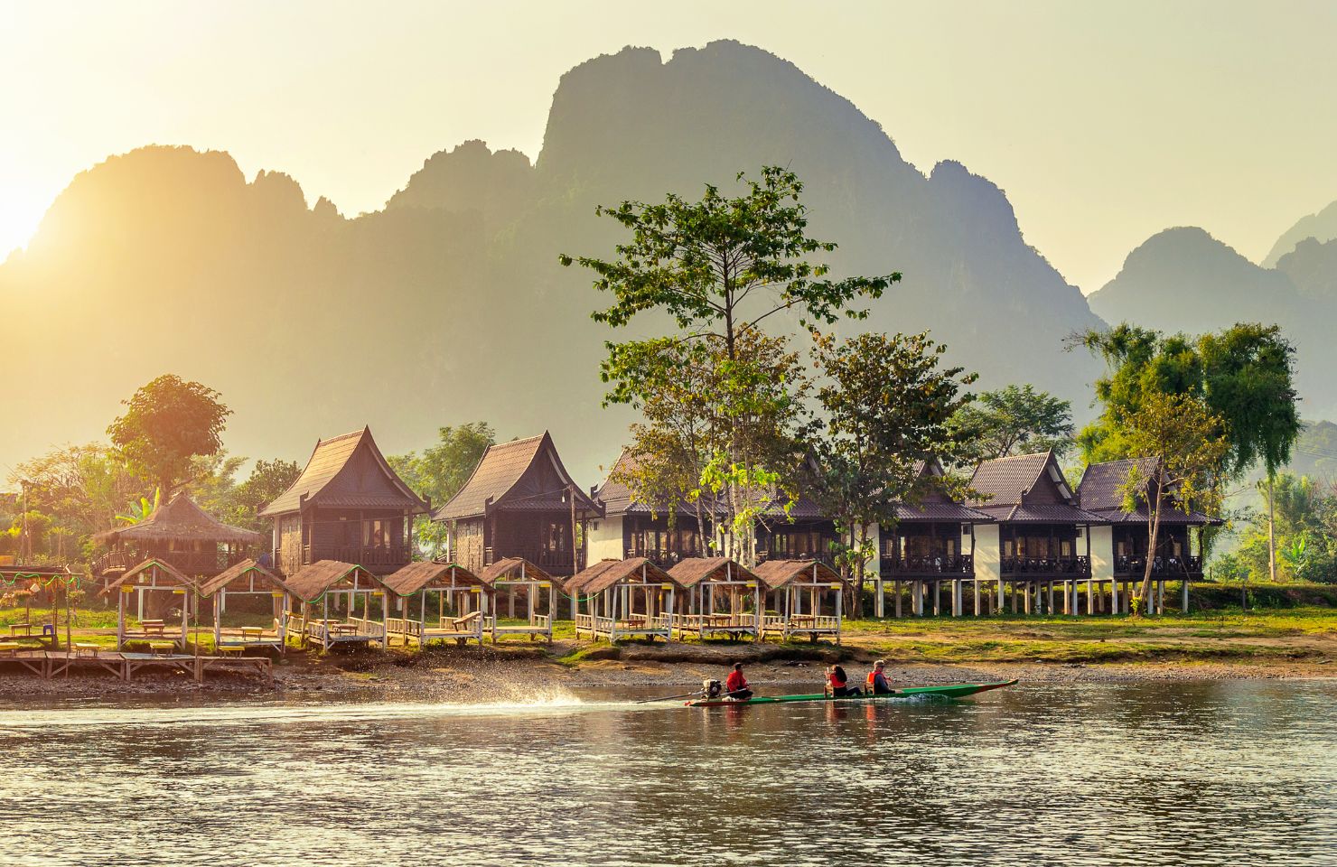 Blick über einen See und auf die Berge und eine Hausreihe in Laos