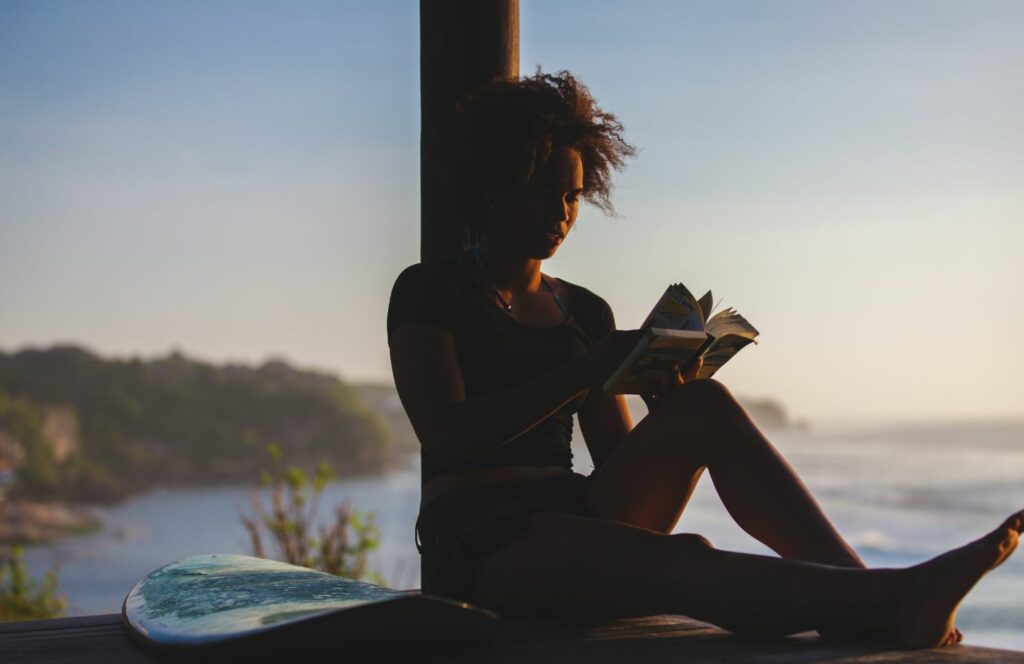 a woman reads a surfing book by the sea in the evening