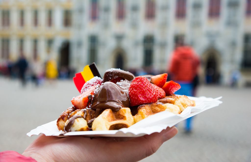 someone holds a traditional Belgian waffle with a flag on it