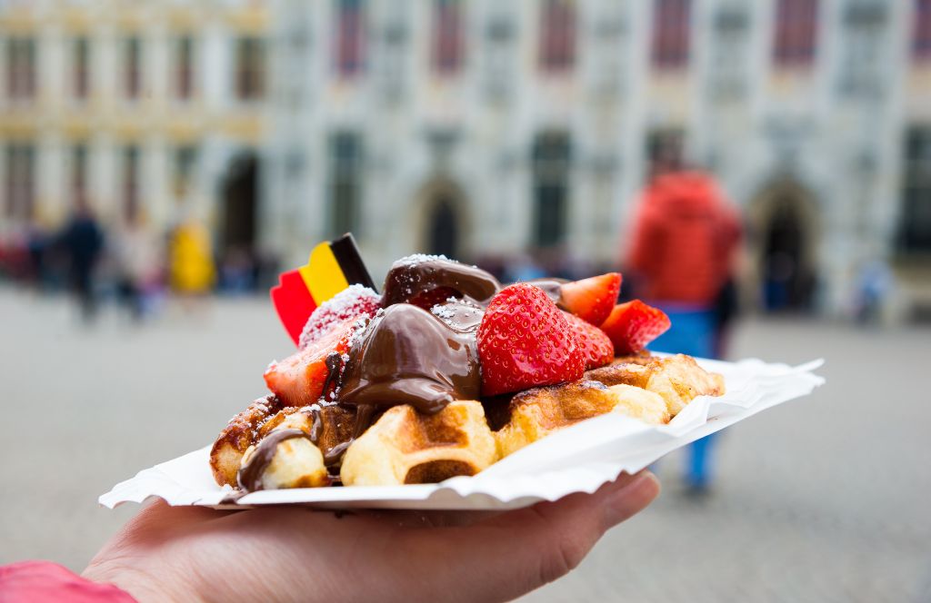 iemand houdt een traditionele Belgische wafel vast met een vlag erop