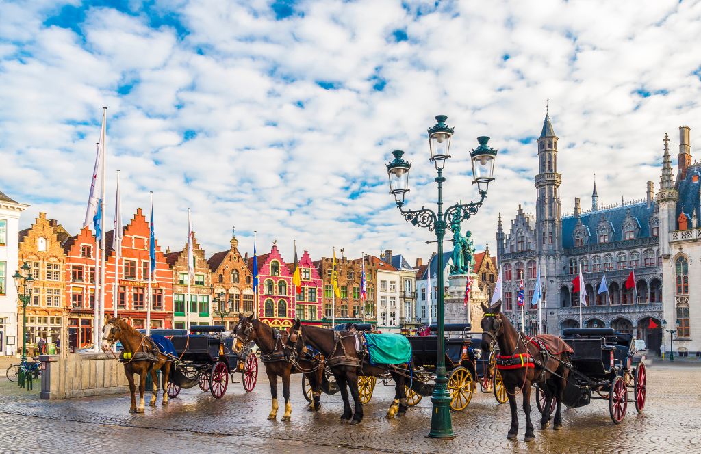 Caballos y carros en la plaza mayor de Brujas, con casas tradicionales y una iglesia al fondo