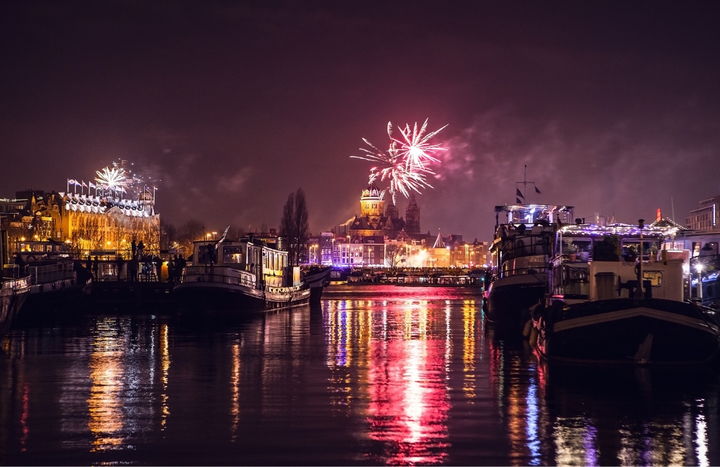 Blick über einen Kanal auf das Feuerwerk über dem Hauptbahnhof von Amsterdam