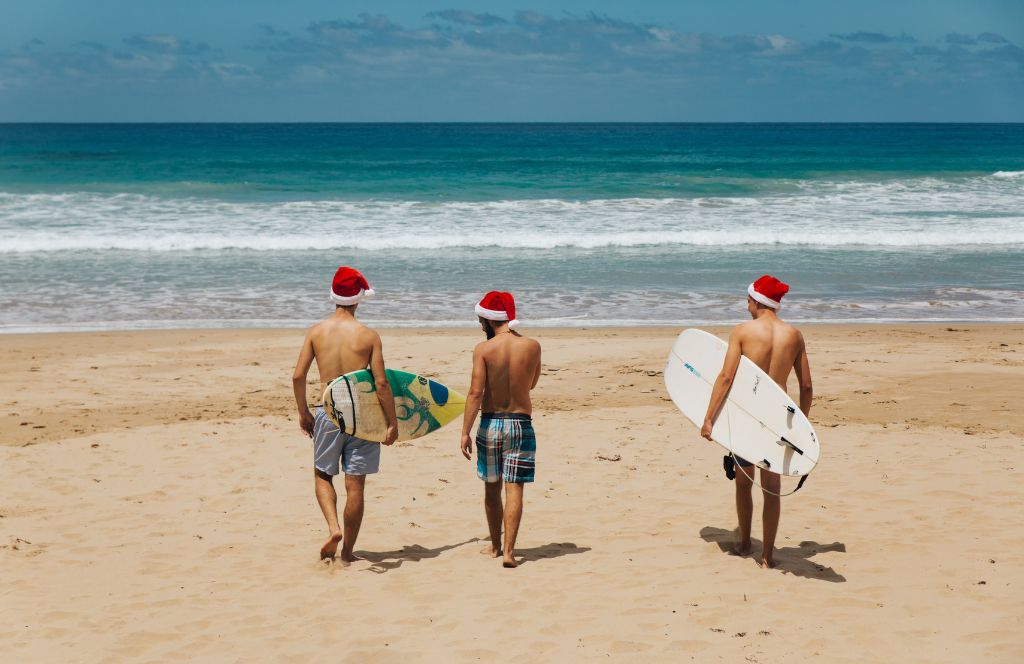 three surfers on the beach at christmas in australia