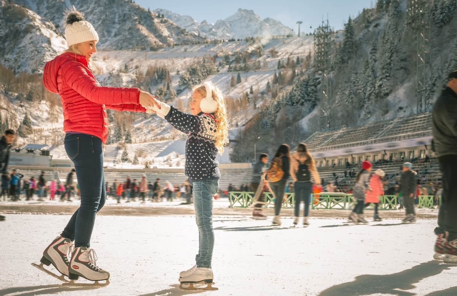 woman and child ice skating under a mountain in the winter